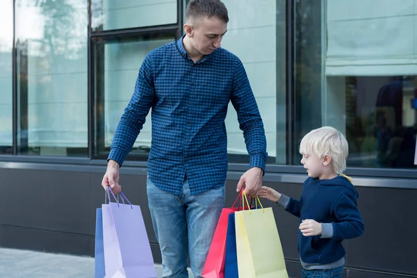 Father and little son with colorful shopping bags on the street. Mall on background