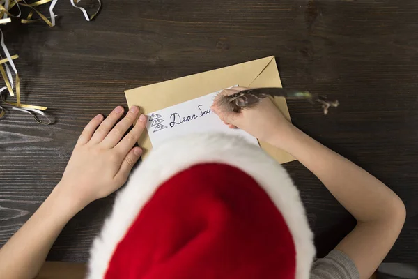 Το παιδί γράφει γράμμα στον Άγιο Βασίλη με το καπέλο του Άη Βασίλη. Στο πάνω μέρος. Χριστουγεννιάτικη ιδέα — Φωτογραφία Αρχείου
