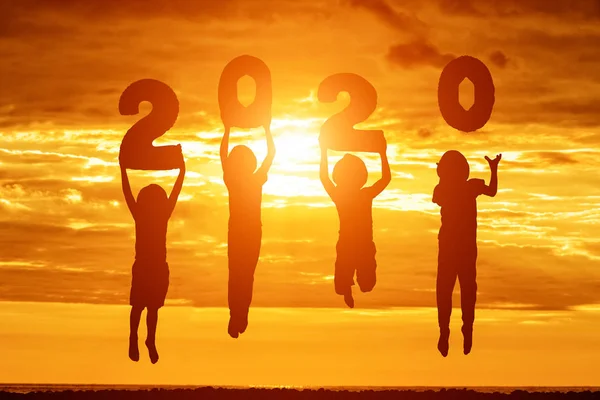 Silhouette of number 2020 in the hands of jumping children. Sunset sky on background. New years concept — Stok fotoğraf