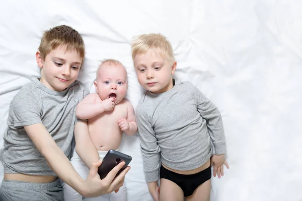 Dos hermanos mayores están acostados con el bebé más joven en una cama blanca. Feliz infancia, gran familia — Foto de Stock