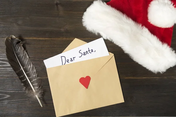 Γράμμα για τον Άγιο Βασίλη σε φάκελο. Στυλό και καπέλο σε ξύλινο φόντο. Χριστουγεννιάτικη ιδέα — Φωτογραφία Αρχείου