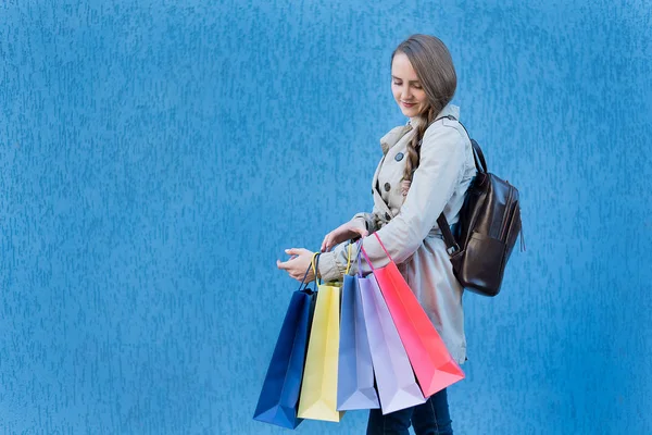 Mujer joven adicta a las compras con bolsas de colores. Pared de calle azul sobre fondo —  Fotos de Stock