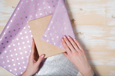 Kadın eli, parlak bir menekşe benekli kağıda bir hediye koyar. Üst görünüm