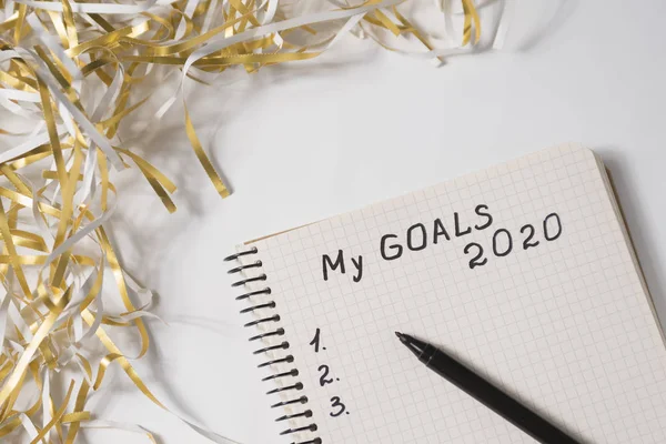 Phrase My Goals 2020 in a notebook, pen. Tinsel on white background. Close up