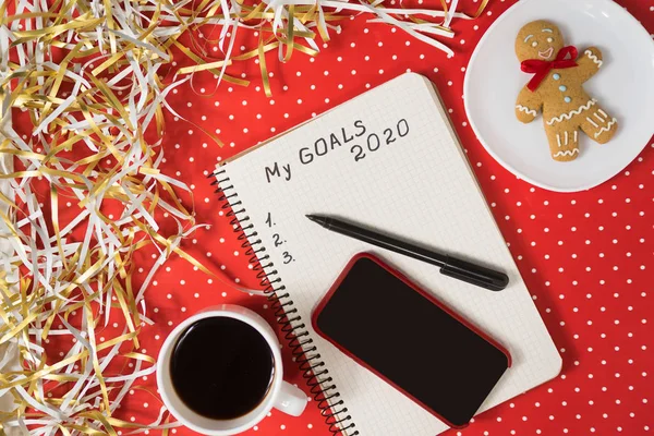 Εκφράσεις τους στόχους μου για το 2020 σε ένα σημειωματάριο, μαύρο στυλό και έξυπνο τηλέφωνο. Μελόψωμο και καφές σε κόκκινο φόντο. — Φωτογραφία Αρχείου