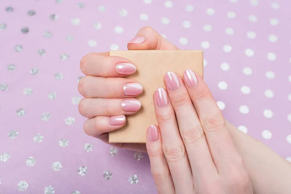 Malá kartónová krabička v ženských rukou. Jemná růžová manikúra. Lilac polka tečka pozadí — Stock fotografie