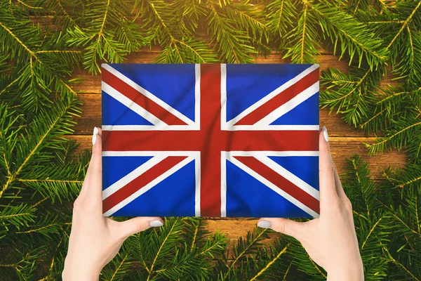 Caixa com bandeira da Grã-Bretanha em mãos femininas. ramos de abeto no fundo — Fotografia de Stock