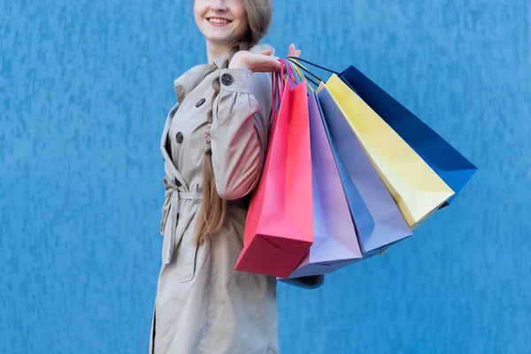 カラフルなバッグで幸せな若い女性のお店。背景の青い通りの壁 — ストック写真