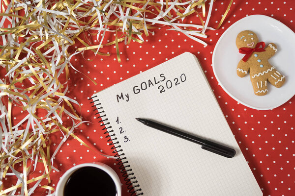 Фраза My Goals 2020 в блокноте, черная ручка. Пряники, кофе на красном фоне. Концепция Нового года
