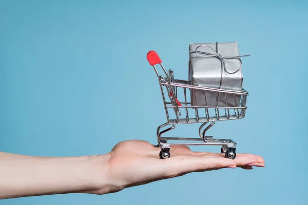Nákupní vozík s dárkem na ženské dlani. Sezóna prodeje a slevy. Detailní záběr — Stock fotografie