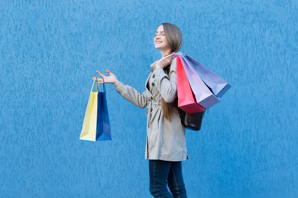 Vrolijke jonge vrouw shopaholic met kleurrijke tassen. Blauwe straatmuur op achtergrond — Stockfoto