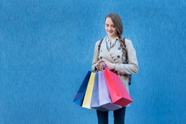 Mujer joven adicta a las compras con bolsas de colores. Pared de calle azul sobre fondo —  Fotos de Stock