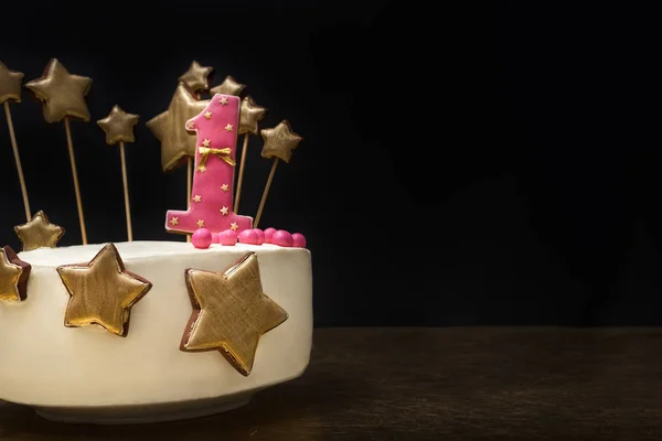 Gâteau d'anniversaire décoré de rose numéro 1 et étoiles dorées de pain d'épice sur un fond sombre . — Photo