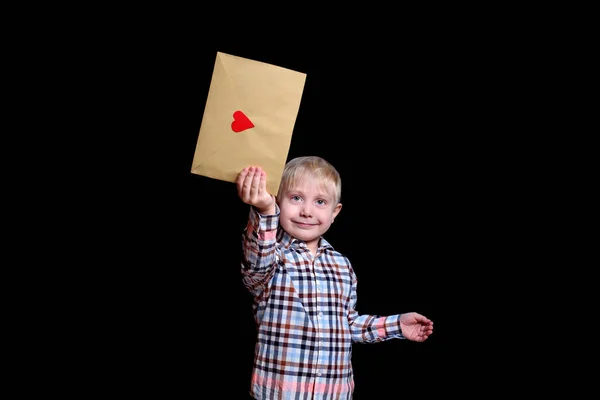 Leuke blonde jongen heeft een envelop met een rood hart. Gefeliciteerd, Valentijnsdag. Zwarte achtergrond — Stockfoto