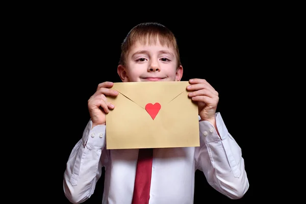 Leuke jongen in een shirt en stropdas houdt een envelop met een hart vast. Isoleer op zwarte achtergrond — Stockfoto