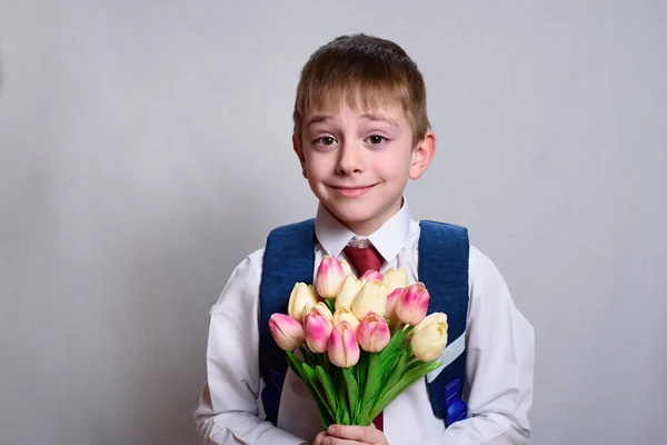 Uczeń z torbą szkolną trzymający bukiet tulipanów. Białe tło — Zdjęcie stockowe