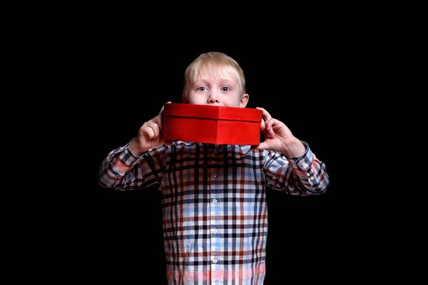 Маленький хлопчик тримає червону коробку у формі серця. Ізольовані на чорному тлі — стокове фото