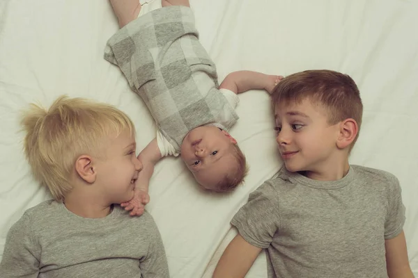 Dos hermanos mayores y el bebé más joven en una cama blanca. Feliz infancia, gran familia. Vista superior — Foto de Stock