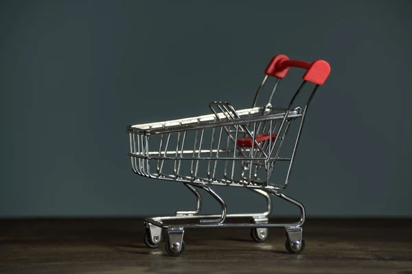 Toy metal shopping trolley on table on a dark background. Side view — Stock Photo, Image