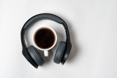 Kablosuz tam boyutlu kulaklıklar ve beyaz arka planda bir fincan kahve. Tam üstte