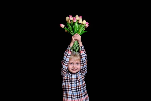 Un garçon blond tient un bouquet de tulipes au-dessus de sa tête. Fond noir — Photo