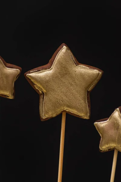 Gold colored star shaped gingerbread cookies on a stick on a black background