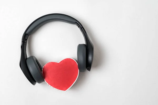 Full-size wireless headphones pulled over small red heart-shaped box on white table. Love music concept. Directly above — Stock Photo, Image