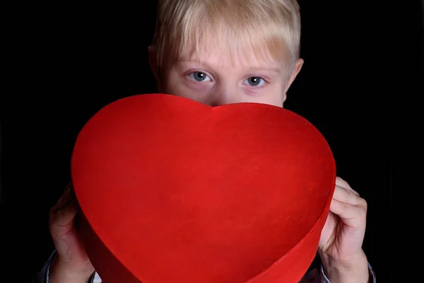 Een blondine met een rode doos in de vorm van een hart op een zwarte achtergrond. Sluiten. — Stockfoto
