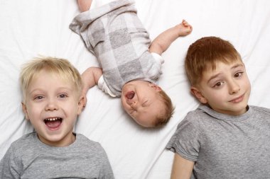 İki büyük kardeş ve en küçük bebek beyaz bir yatakta. Mutlu çocukluk, büyük aile. Üst görünüm