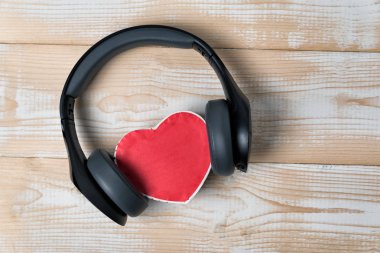 Tam boyutlu kablosuz kulaklıklar açık kahverengi tahta bir masada kırmızı kalp şeklinde küçük bir kutuyu kenara çekti. Müzik konseptine bayılırım. Tam üstte