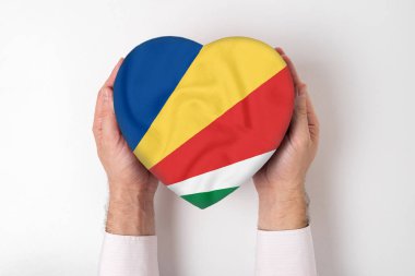 Kalp şeklinde bir kutuda, bir erkeğin ellerinde Seyşel bayrağı. Beyaz arkaplan