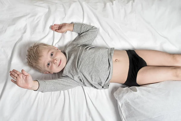 Blond pojke som ligger på det vita lakanet. Vakna på morgonen glad. Höga fem — Stockfoto