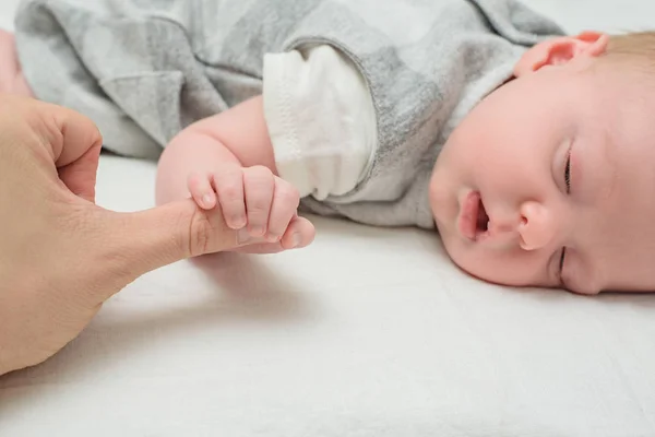 Barnet håller i fingret på en vuxen. Ta hand om den nyfödde. Närbild, vit bakgrund — Stockfoto