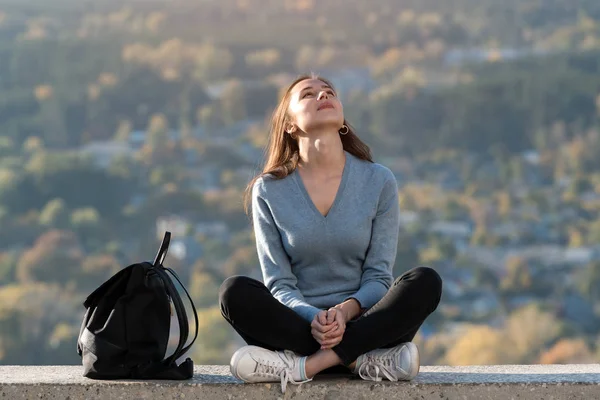 Ung kvinna sitter i naturen tittar på himlen och njuter av livet. Framifrån — Stockfoto