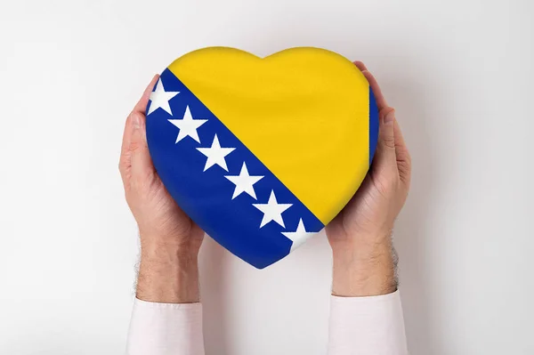 Bandera de Bosnia y Herzegovina en una caja en forma de corazón en manos masculinas. Fondo blanco — Foto de Stock