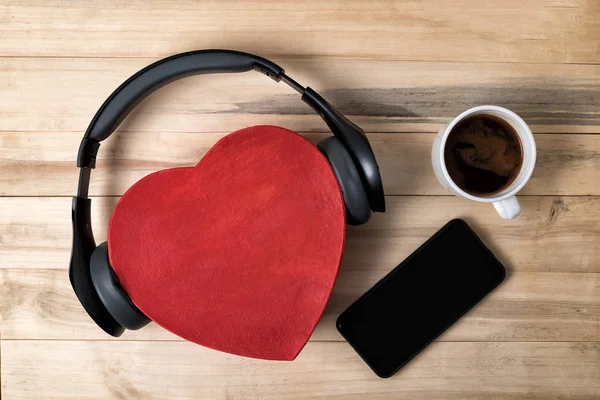 木製の背景にヘッドフォン、スマートフォンやコーヒーと赤のハート形の箱。音楽と愛の概念. — ストック写真