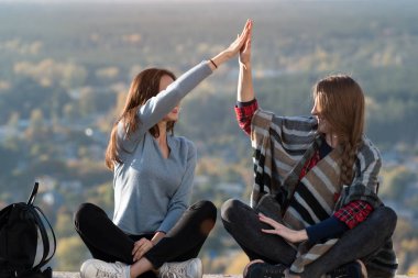 Çak bakalım. Doğanın arka planında oturan iki kız. Bir arkadaşla seyahat et. Ön görünüm