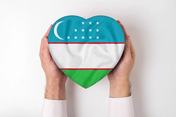 Σημαία του Ουζμπεκιστάν σε ένα κουτί σε σχήμα καρδιάς σε αρσενικά χέρια. Λευκό φόντο — Φωτογραφία Αρχείου