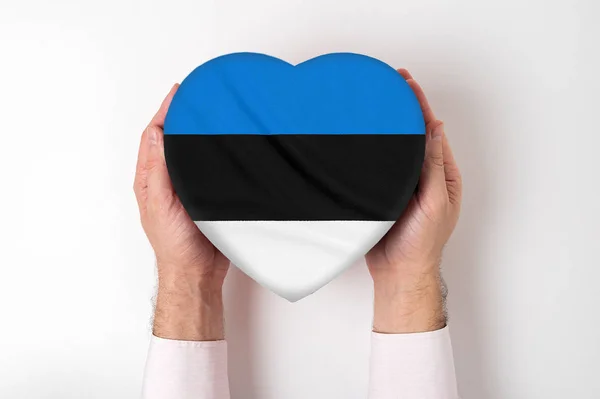 Bandeira da Estônia em uma caixa em forma de coração em mãos masculinas. Fundo branco — Fotografia de Stock