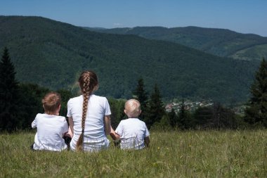 Anne ve çocuklar çayırda dinleniyor. Yolculuk boyunca çocuklu dadı. Arka plan