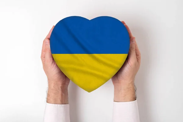 Bandeira da Ucrânia em uma caixa em forma de coração em mãos masculinas. Fundo branco — Fotografia de Stock