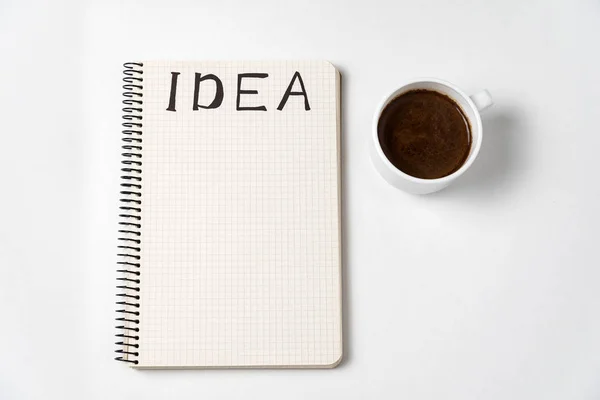 Notitieblok met woord idee en een kopje koffie op witte achtergrond. Creatieve ideeën en plannen. Kopieerruimte — Stockfoto
