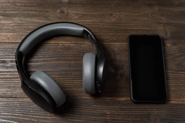 Teléfono y auriculares sobre fondo de madera. Escuchar música y audiolibros . —  Fotos de Stock