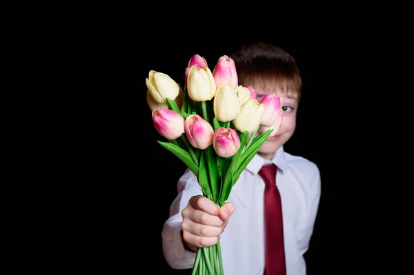Lindo chico con camisa blanca da un ramo de tulipanes. Aislar sobre fondo negro — Foto de Stock