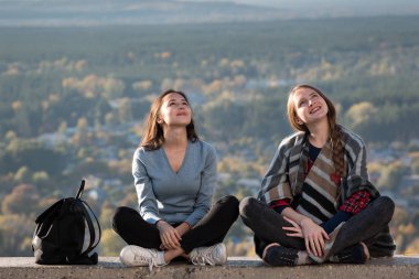 Doğanın arka planında oturan ve gülümseyen iki genç kız. Arkadaşla tatil, tatiller. Ön görünüm