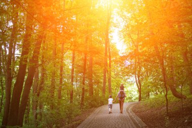Güneşli bir günde parkta yürüyen çocuklu bir baba. Ailenle yürü.