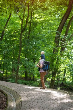 Baba ve oğul parkta yürüyor. Çocuk babasının omuzlarında. Arka plan dikey çerçevesi.
