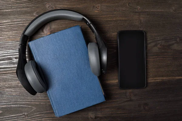 Teléfono móvil y libro con auriculares sobre fondo de madera. Concepto de audiolibro. Vista superior, espacio de copia . —  Fotos de Stock