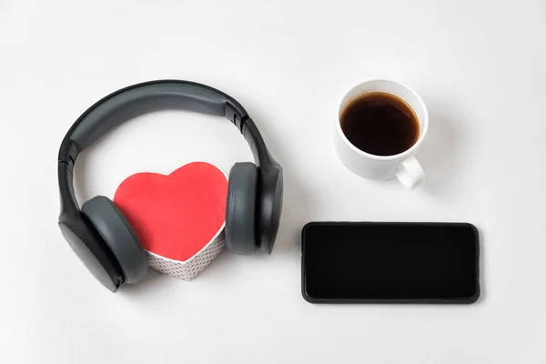 Black headphones and heart shape box, smartphone and cup of coffee. White background copy space