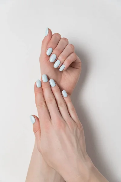 Kvinnliga händer med delikat blå manikyr. Gel polska. Vit bakgrund. Vertikal ram — Stockfoto